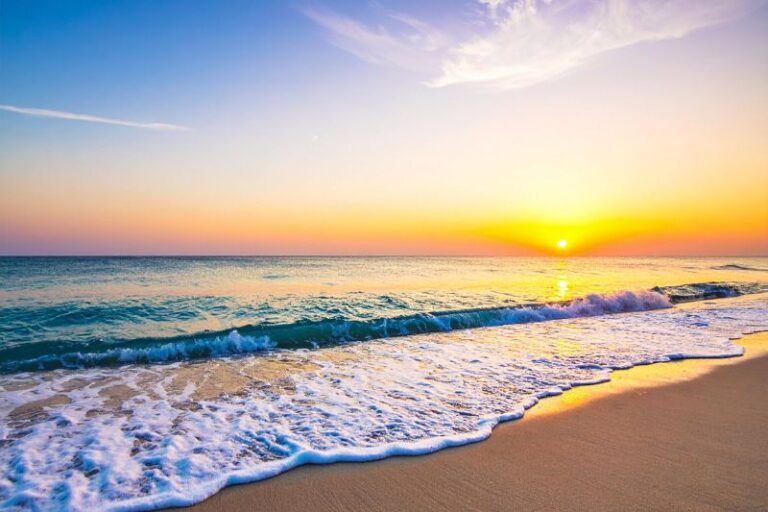 Ein friedlicher Sonnenaufgang an einem weiten Sandstrand mit sanften Wellen, der die innere Klarheit und das Setzen gesunder Grenzen durch eine professionelle NARM-Therapie symbolisiert.
