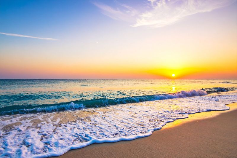 Ein friedlicher Sonnenaufgang an einem weiten Sandstrand mit sanften Wellen, der die innere Klarheit und das Setzen gesunder Grenzen durch eine professionelle NARM-Therapie symbolisiert.