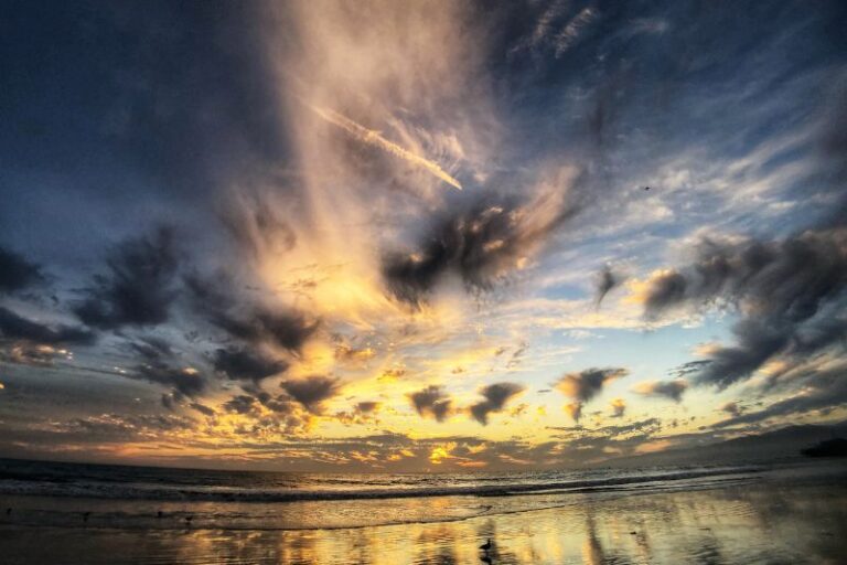 Ein dramatischer Wolkenhimmel über dem Meer bricht auf und lässt goldenes Sonnenlicht auf den Strand fallen, als Symbol für Hoffnung und den mutigen ersten Schritt in eine Psychotherapie.