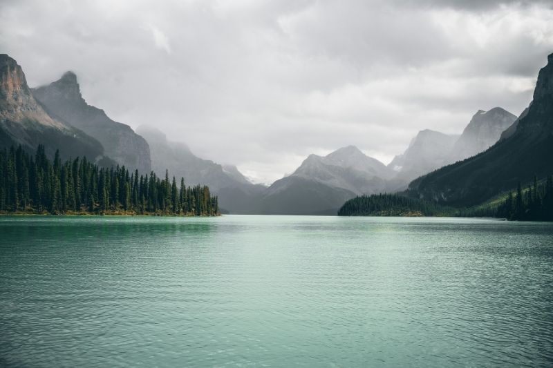Ein ruhiger Bergsee umgeben von dichten Wäldern und nebelverhangenen Bergen, der die emotionale Stille und den Weg zur Hilfe bei Depressionen in Kiel symbolisiert.